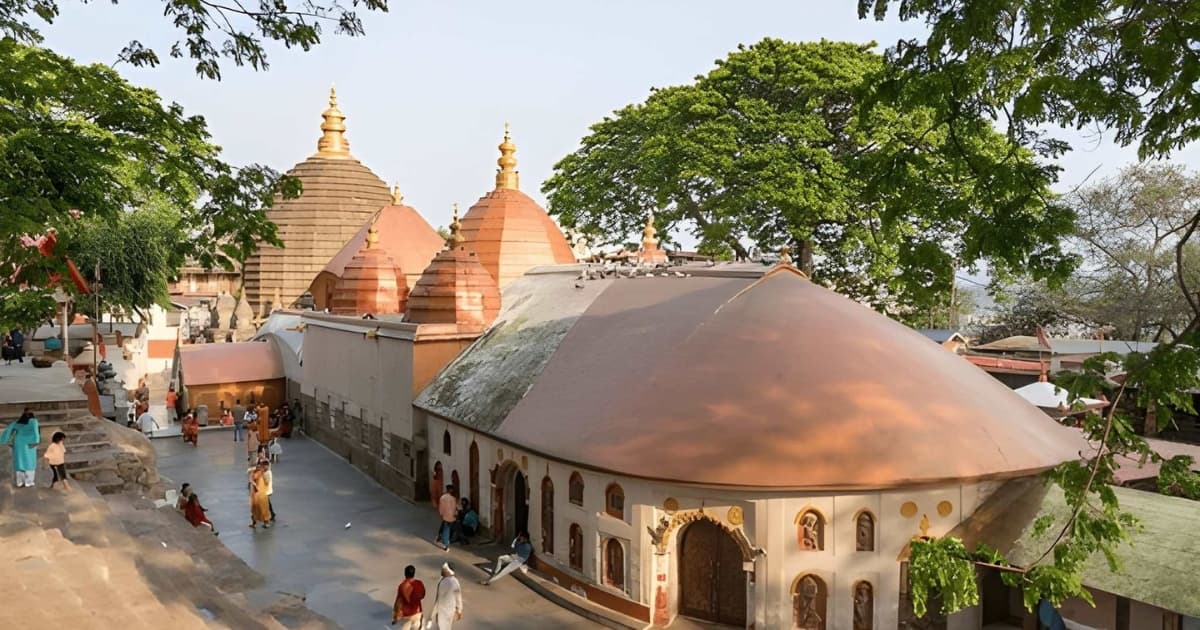 An elevated view of the historic Kamakhya Mandir in Guwahati, Assam, showcasing its unique terracotta-colored domed architecture, spacious courtyards filled with devotees, and beautiful lush green surroundings.